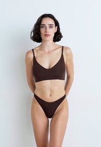 Bralette marron sans couture avec des bretelles fines et un décolleté en V, associé à un string minimaliste assorti, les deux ayant une texture lisse.