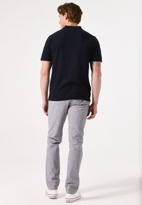 Marineblaues Poloshirt mit kurzen Ärmeln, strukturierter Stoff;hellgraue maßgeschneiderte Hose; weiße Sneakers; von hinten gesehen.