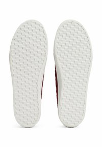 Parte superior del zapato texturizada en rojo con suelas de goma blanca. Las suelas presentan un patrón de rejilla para mayor agarre, con bordes redondeados y construcción sin costuras.