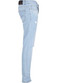 Jeans de denim azul claro con un corte ajustado, que presentan detalles desgastados y decoloración. La tela tiene una textura ligeramente usada y un diseño clásico de cinco bolsillos.