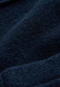 Tumed sinine tekstureeritud kangas pehme karvase pinnaga ning õrnade voltidega, mis loovad leebeid varje ja esiletõsteid.