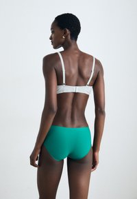 Sutien gri deschis cu bretele ajustabile, asociat cu pantaloni scurți verzi. Textură netedă, design minimalist și un croi pe talie joasă vizibil din spate.