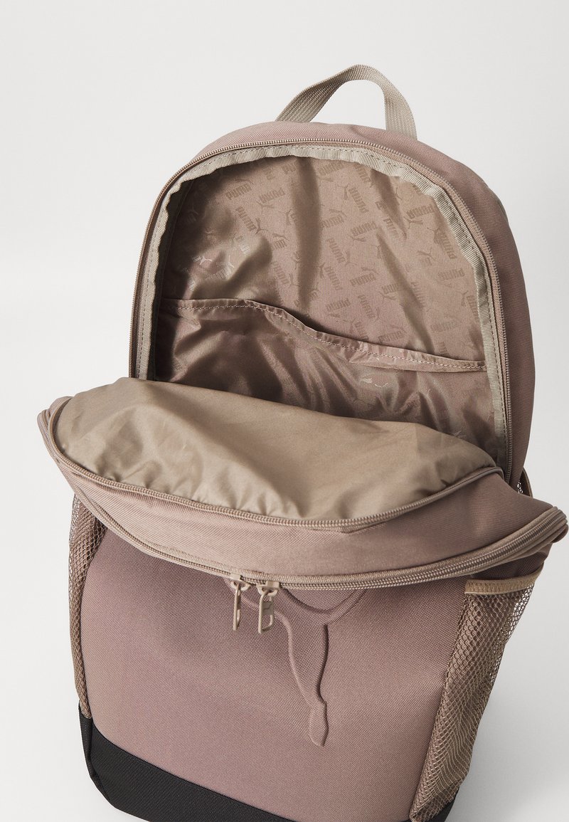 Zaino marrone con apertura a zip, rivestimento interno beige, tasca frontale in rete e motivo logo delicato all'interno.