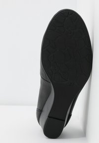 Chaussure en cuir noir avec un design courbé, semelle plate et fond en caoutchouc texturé. Présente une indication de taille "37" et un motif ressemblant à une surface craquelée.