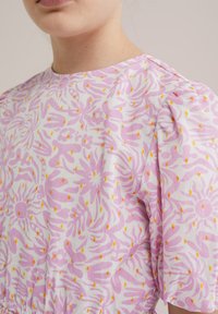 Kortärmad blus i vit bomull med rosa abstrakt blommönster och gula detaljer, med rund hals och rynkad ärm.