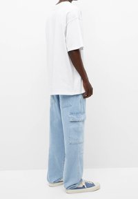 T-shirt de algodón blanco de gran tamaño, jeans cargo azul claro con múltiples bolsillos y sneakers azules y beiges.