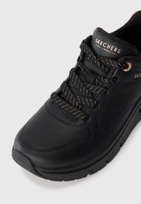 Sneaker in pelle nera con tomaia texturizzata, punta rinforzata, dettagli oro a contrasto sull'hardware e lacci rotondi. Logo posizionato sulla linguetta.