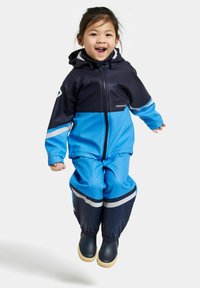 Blå och marinblå vattentät overall med huva, utrustad med reflexränder och elastiska muddar, kombinerad med svarta gummistövlar.