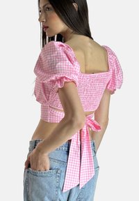 Rosa Gingham-Crop-Top mit Puffärmeln, gerafftem Oberteil und einer Schleife an der Taille. Getragen mit hochtaillierten Denimshorts.