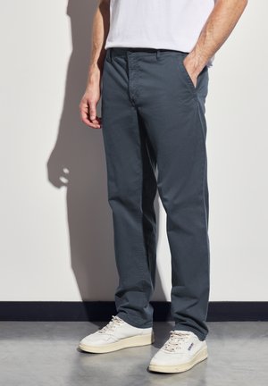 Pantalons en coton gris foncé avec une coupe décontractée, dotés de poches latérales et d'une texture lisse, associés à des baskets blanches.
