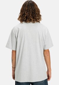 Šedé bavlněné tričko s volným střihem a krátkými rukávy, které má jednoduchý design bez grafik a vzorů. Zobrazeno ze zadní strany.