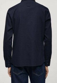 Camicia a maniche lunghe blu navy realizzata in tessuto testurizzato, con orlo dritto e polsini con bottoni. Sul retro presenta un yoke e un gancio per appenderla.