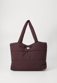 Gestepptes Tote-Bag in tiefem Burgundy, mit zwei stabilen Griffen und einem einfachen Logo-Tag. Weicher, strukturierter Stoff mit horizontaler Naht.