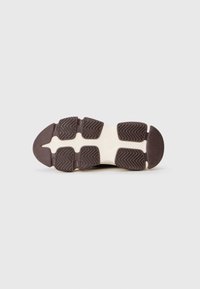 Semelle de sneaker en caoutchouc avec un motif de texture, affichant une couleur marron foncé et de prominents motifs en zigzag pour une meilleure adhérence. Bord courbé au niveau des orteils.