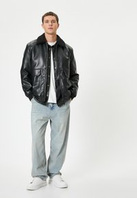 Chaqueta de cuero negra con cuello de piel sintética, dos bolsillos delanteros, combinada con pantalones vaqueros claros y holgados y zapatillas blancas.