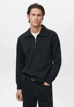 Pullover negro con cuello tipo cremallera, hecho de un material suave, con mangas largas y un corte holgado. El cuello es estructurado y cuenta con un cierre de cremallera.