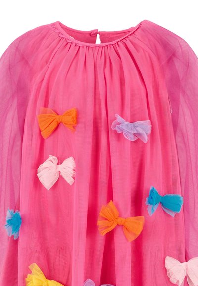 Różowa suknia z tiulu o płynnej formie, z kolorowymi warstwowymi kokardami w odcieniach pomarańczowym, różowym, niebieskim i żółtym przyszytymi w różnych miejscach.