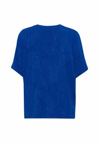 Top de manga corta azul en un tejido texturizado que presenta un intrincado patrón floral. Corte holgado con escote redondo y dobladillo recto.