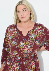 Vestido floral burdeos con mangas tres cuartos y escote en V. Presenta un patrón floral multicolor, tejido ligero y cintura fruncida.