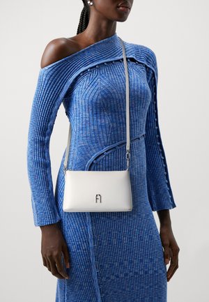 Woman in a blue ribbed knit dress with buttons, carrying a small white crossbody bag with a silver logo on the front.