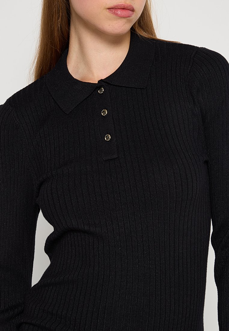 Polo shirt nera a coste con colletto classico e tre bottoni dorati sul davanti. Il tessuto sembra strutturato e aderente.