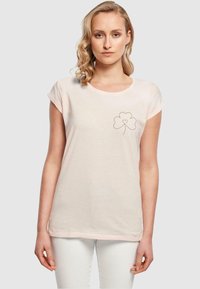 Lys rosa bomull t-skjorte med rullede ermer, rund hals, og et lite svart brodert kløverdesign på venstre bryst.