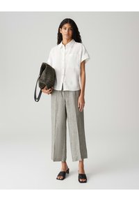 Witte linnen shirt met korte mouwen en een voorkennis, gecombineerd met lichtgrijze wijde linnen broeken, zwarte instapsandalen en een gestructureerde donkere tas.