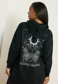 Felpa nera con un design grafico di mani, un sole e rose in bianco, con il testo "CELESTIAL DREAMER" sottostante.