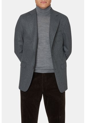Grå ullkavaj med slag och två framfickor, stängs med en knapp, över en ljusgrå polotröja, kombinerad med bruna manchesterbyxor.