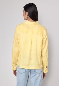 Camicia di lino gialla con maniche lunghe, dalla texture sottile e dal taglio morbido. Presenta un yoke posteriore e chiusure a bottone ai polsini.