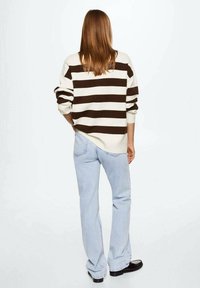 Pull crème oversize à rayures marron, manches retroussées, associé à un jean évasé bleu clair et des chaussures noires, vu de dos.