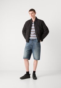 Svart quiltet bomberjakke, grå og hvit stripete t-skjorte, denimshorts og svarte sneakers med matchende sokker. Enkelt, uformelt antrekk.