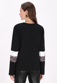 Schwarzes Langarmshirt mit weißen und Leopardenmuster-Streifen an den Ärmeln; glatter Stoff, lockere Passform und Rundhalsausschnitt.