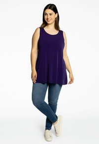 Lilla ærmeløs top med rund halsudskæring, udvidet design, parret med medium blå jeans og hvide sneakers. Glat, letvægtsstof.