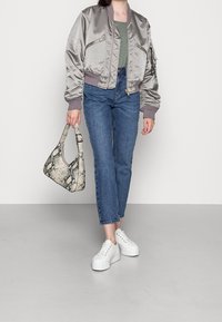 Hopeinen bombertakki vetoketjullisilla taskuilla, yhdistetty sinisiin suoralahkeisiin farkkuihin ja valkoisiin korollisiin tennareihin. Asustettu käärmekuvioisella käsilaukulla.