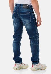Dunkelblaue Denim-Jeans mit schmalem Schnitt, die über ausgefranste Details, mehrere Taschen und einen markierten Taillenbund auf der Rückseite verfügen.