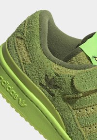 Detailní záběr na zelenou tenisku Adidas s texturovaným semišovým svrškem, embosovaným logem na podrážce a polstrovaným límcem a jazykem.