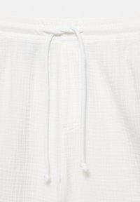 Pantalon blanc en tissu texturé avec une taille élastique et un cordon noué au centre devant.