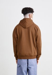 Sudadera marrón con capucha y puños acanalados, con una textura suave. Combinada con pantalones cargo de color azul claro.