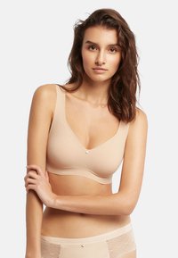 Sujetador beige sin costuras con un diseño en V, textura suave, tirantes anchos y un pequeño detalle decorativo en el centro. Combínalo con braguitas beige a juego.