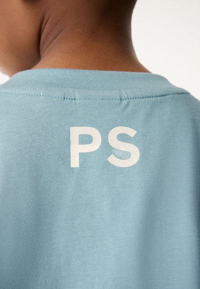 Gaiši zila kokvilnas T-kreklu ar apaļu apkakli un baltu "PS" uzdrukātu aizmugurē. Gluda tekstūra ar īsām piedurknēm.
