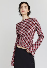 Top a maniche lunghe a quadri rossi e bianchi con scollatura a barca e polsini svasati, abbinato a una gonna nera con dettagli ad anello.