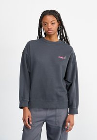 Kullsvart sweatshirt med ribbestrikkede mansjetter og kant, med rosa "ROXY" tekst og en kaktusgrafikk på brystet. Avslappet passform.