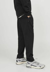 Black sweatpants with a smooth texture and side zip pockets, paired with gray athletic shoes featuring a mesh design and white soles.
