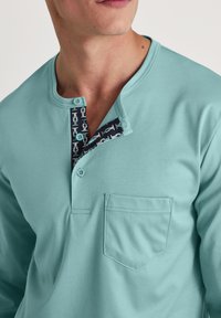 Lichtblauwe longsleeve shirt met een pocket en een contrasterende marineblauwe knoopsluiting met een geometrisch patroon en twee zichtbare knopen.