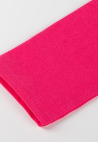 Manche en tissu rose vif avec coutures visibles sur fond blanc, mettant en valeur la texture du textile et le détail de l’ourlet.