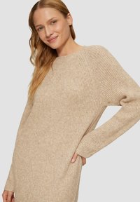 Beige gebreide trui met een ontspannen pasvorm, geribbelde textuur, ronde halslijn en lange mouwen. Heeft zijzakken voor extra detail.
