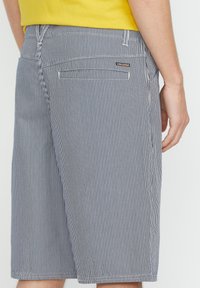 Striped shorts in navy blue and white with a relaxed fit. Features back pockets and a branded patch. Soft fabric, knee-length design.