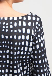 Robe en tissu noir avec un motif de formes irrégulières blanches et bleu clair, col rond et texture lisse.