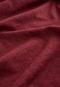 Bordeauxrood textiel met een zachte, gestructureerde weving, met zachte plooien en een licht verweerde, gemêleerde uitstraling.